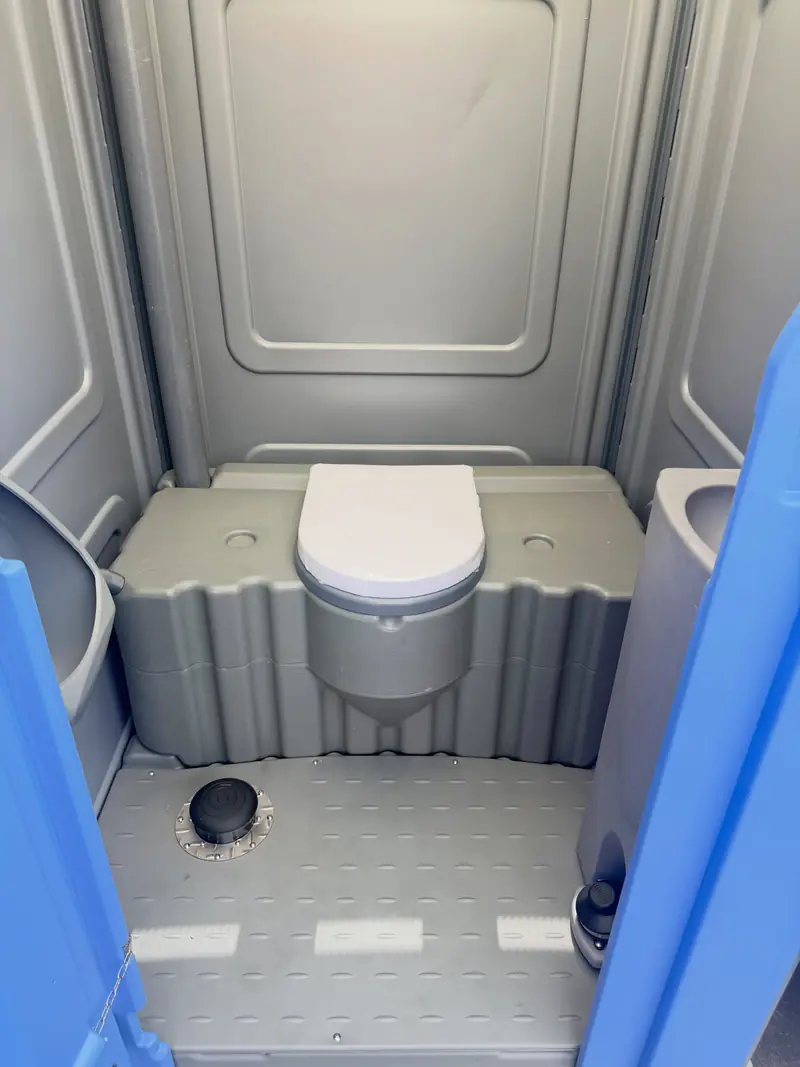 Inside a clean standard porta potty with seat and urinal