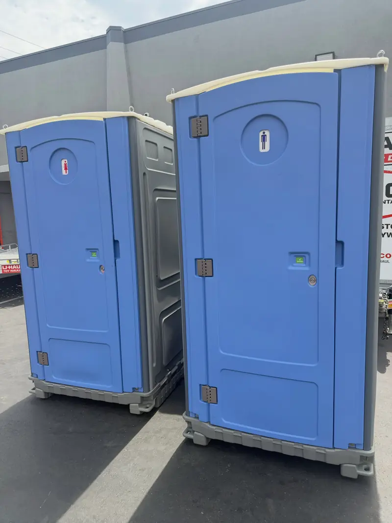 Two blue standard porta potties set against a building in Lancaster, PA